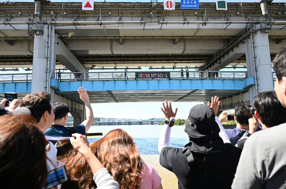 주말 한강버스에 오른 시민들이 반포대교 아래를 지나며 다리 위 시민들과 손을 흔들며 즐거운 시간을 보내고 있다.